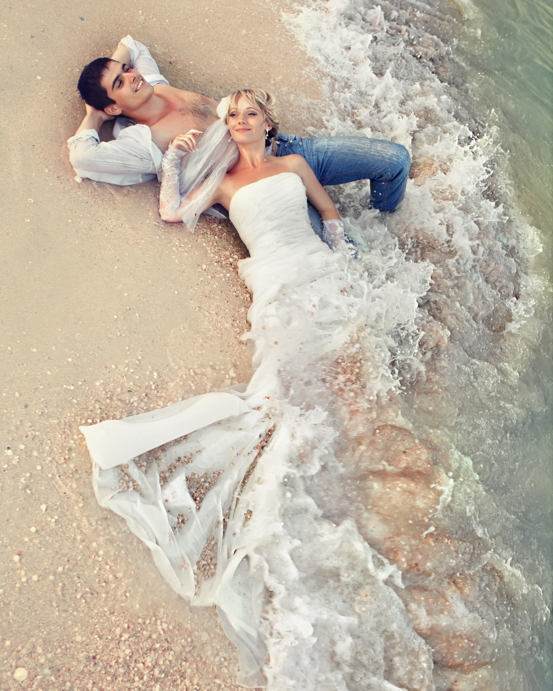 trash wedding dress photoshoot of bride and groom lying in beach